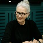 Elderly woman with gray hair wearing eyeglasses during a business meeting indoors.