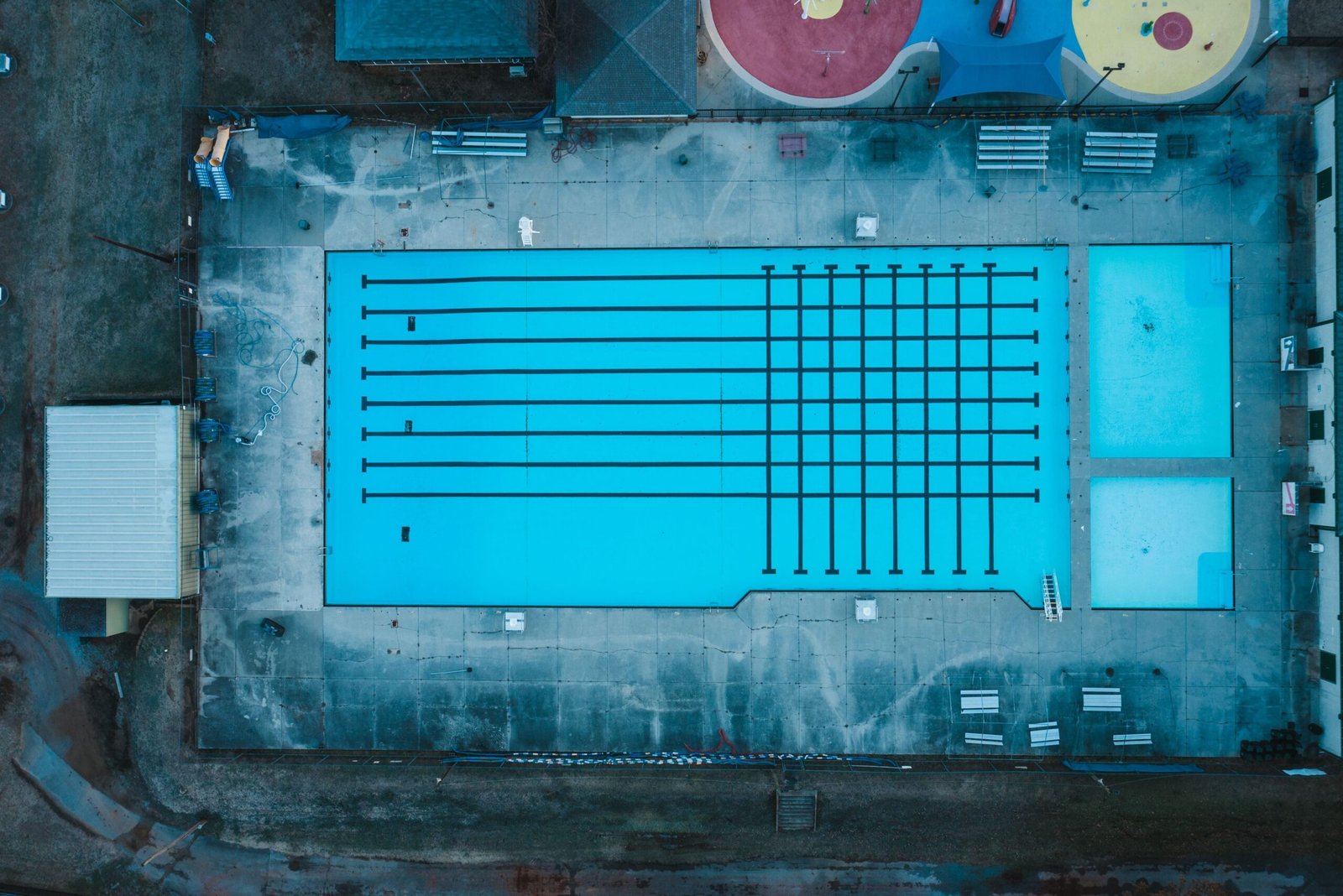Aerial view of empty outdoor swimming pool and small house located in suburban area of city in daytime
